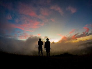 Silhouettes of two campers watching the sunrise in the mist from top of 'Le Pouce' mountain