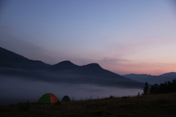 Picturesque view of mountain landscape with thick fog and camping tents at sunset