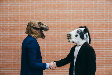 Men shake hands with dinosaur and cow masks.