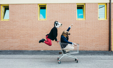 Two men in animal masks have fun with the shopping cart.