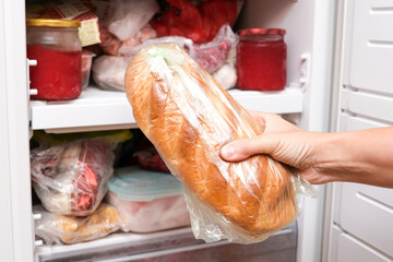 A hand putting a loaf of wheat bread in reserve on a shelf of a home freezer, long life food...