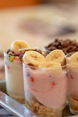 Yogurt dessert with different fruits, crushed cookie and chocolate, presented in crystal glasses decorated with floral elements.