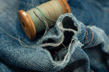 Hole in jeans. Needle with thread for darning jeans. Tools for work dressmaker, seamstress fashion designer - obrazy, fototapety, plakaty