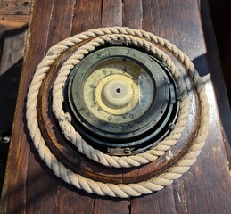 An old ship's compass on a sailboat next to the helm and a nautical rope twisted around
