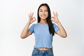 Cute asian girl winking and smiling, showing okay, ok zero gesture, confirm something is good, recommending product, white background