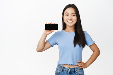 Smiling cute brunette woman showing horizontal smartphone screen, demonstrating app interface on phone, white background