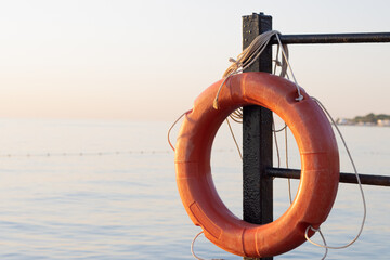 orange lifebuoy hanging on a metal fence against the background of the sea