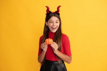 happy halloween. devil kid with pumpkin. trick or treat. teen girl on yellow background.