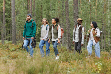 Diverse group of young people walking in forest with backpacks while exploring hiking trails, copy...