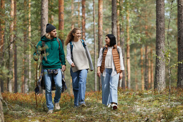 Full length portrait of young people walking in forest with backpacks while enjoying hiking trails,...
