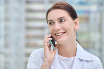 Smiling woman in white coat communicating by smartphone