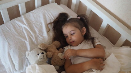 little cute girl is going to go to bed. indulges in, does not want to sleep. naughty. Cute little girl sleeping with teddy bear in bed