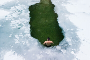 One man in water hole of icy water covered with white snow and ice practicing cold water therapy, 