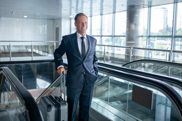 Joyful successful man with suitcase on escalator