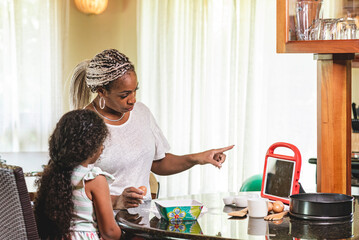 Madre e hija afroamericanas preparando comida mientras siguen una receta en la tableta
