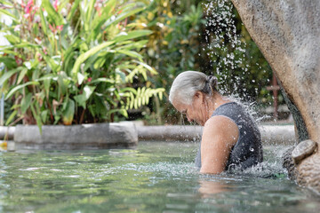 Mujer adulta mayor con cabello canoso en una piscina de agua termal disfrutando mientras cae agua sobre su espalda