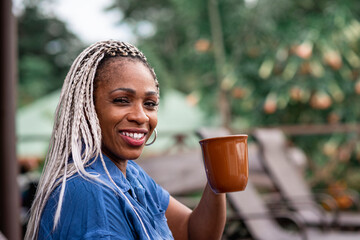 Mujer madura afroamericana con cabello con trenzas sonriendo mientras bebe un café