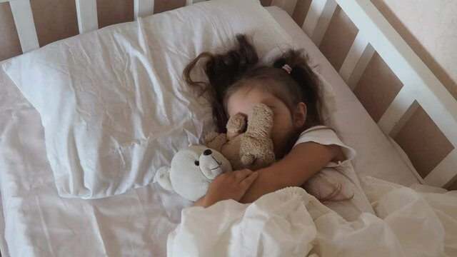 little cute girl is going to go to bed. indulges in, does not want to sleep. naughty. Cute little girl sleeping with teddy bear in bed