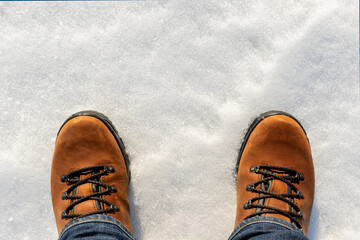 Closeup top above view of male legs in jeans and brown leather warm boots isolated on white icy snow surface background. Detail waterproof shoes. Winter walking and hiking wild nature outdoor concept