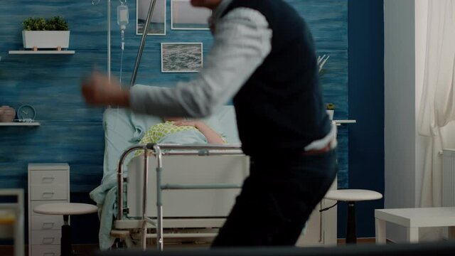 Worried man calling for medical assistance while woman breathing heavy in hospital bed. Doctor and nurse rushing to help retired patient with disease for healthcare in nursing home.