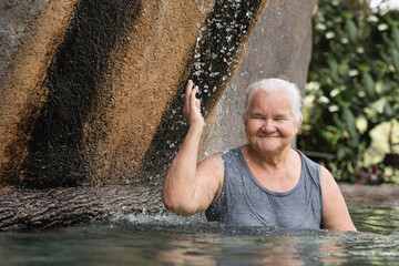 Beautiful smiling old lady enjoying a natural hot spring pool. 
