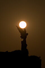 The sun rising over the sculpture of an Angel in Comillas,Cantabria, Spain