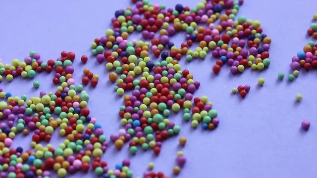 Many colorful foam balls scattered on a purple background. Round multi-color confetti backdrop. Confectionery sprinkles. Festive background. Carnival, celebration new year, anniversary, party concept.