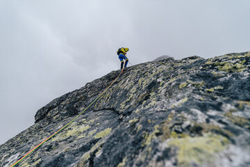 Climber or alpinist rapelling down a high rock wall. Mountainer abseiling on a climbing rope in the...