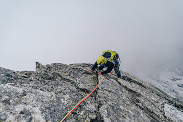 An alpinist or climber climbing high rock face od Piz Badile, Bergell. Climber above clouds on an extreme sport adventure in the mountains.