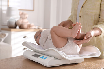 Young woman weighting her cute baby at home, closeup. Health care