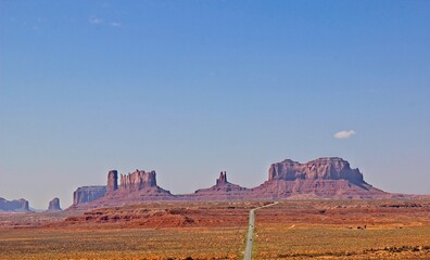 Long Road Leading To Outcropping Mountains In Monument Valley, Utah