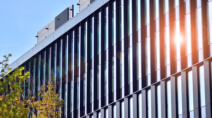 Obraz premium Inspiring view of the modern city. The wall of the building of glass and metal against trees. Corporate construction and ecology, view of modern building with blue sky and green tree. Sunlight