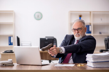 Old businessman holding gun at workplace