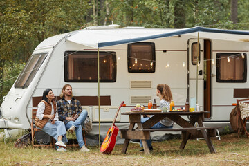 Wide angle view of friends enjoying outdoors while camping with van in forest, copy space