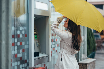 oman holding a yellow umbrella while using the atm machine
