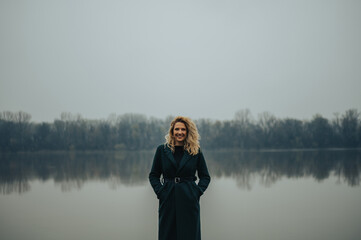 Young blonde woman standing near the river in a green coat
