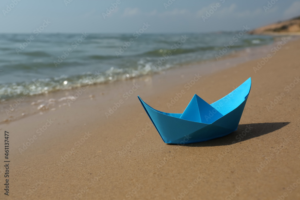 Poster Blue paper boat on sandy beach near sea, space for text