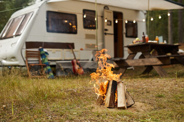 Background image of campfire in forest with trailer van in background, copy space - obrazy, fototapety, plakaty