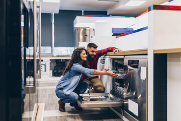 Beautiful and happy young couple buying dishwasher in modern appliances store. - 461137461