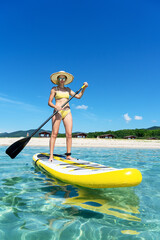 Tanned tourist female in straw hat standing on surfboard with paddle enjoying sup surfing