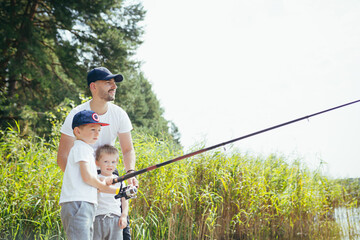 A father with two young sons fishes on the lake in the summer on weekends