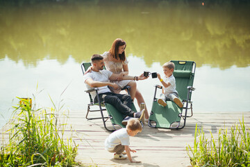 Happy young family with toddler children resting sitting on folding camping chairs over lake on a...