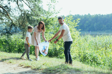 family volunteer cleans garbage in nature. Father and mother, parents, children, son family volunteers in a sunny day cleaning up the rubbish waste bottles in forest of debri folding in plastic bag