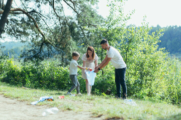 family volunteer cleans garbage in nature. Father and mother, parents, children, son family volunteers in a sunny day cleaning up the rubbish waste bottles in forest of debri folding in plastic bag