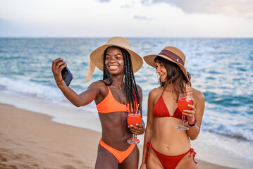 Joyful girlfriends with smartphone taking selfie on beach