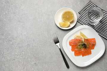 Salmon carpaccio with capers, microgreens and lemon served on grey table, flat lay. Space for text
