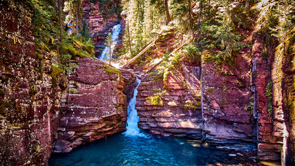 Deep gorge of lichen-covered red rocks with layers of waterfalls