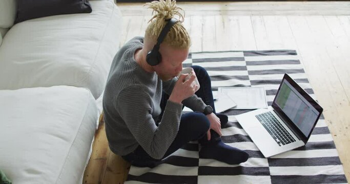 Albino african american man with dreadlocks siting on the floor, working and using laptop
