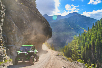 Four Wheel vehicle driving down narrow dirt road in mountains