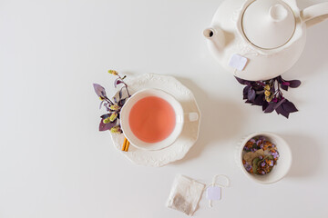 Cup of ginger tea composition with teapot, tea bag and purple leafs on white background. Flat lay, top view. 